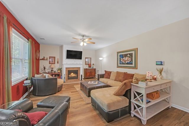 living room with baseboards, a ceiling fan, visible vents, a tile fireplace, and wood finished floors