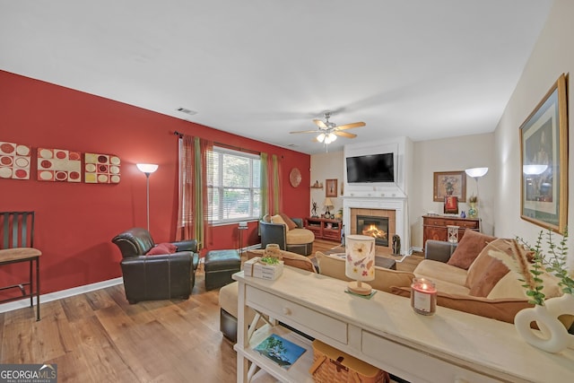 living room featuring a tiled fireplace, visible vents, ceiling fan, and wood finished floors