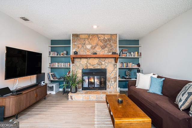 living room with a textured ceiling, wood finished floors, built in shelves, and a stone fireplace