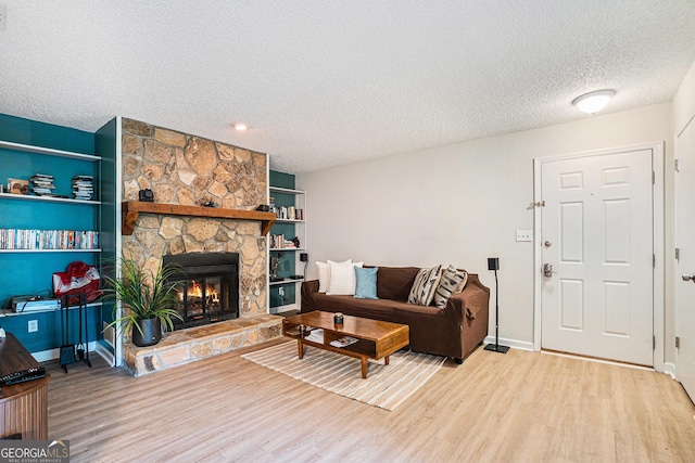 living area featuring a textured ceiling, wood finished floors, a stone fireplace, and baseboards