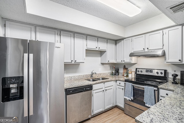kitchen featuring stainless steel appliances, under cabinet range hood, a sink, light wood-style floors, and a textured ceiling