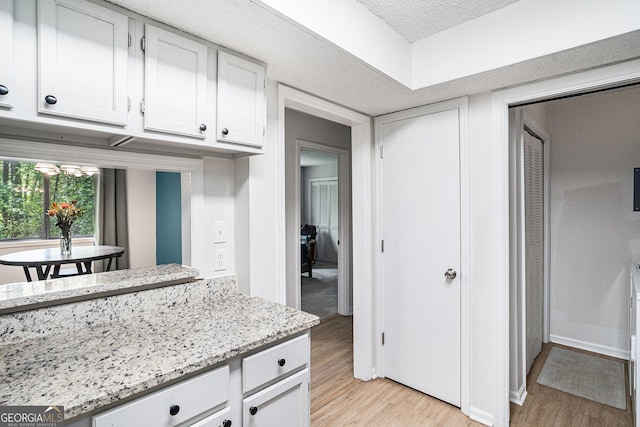 kitchen featuring light wood finished floors, white cabinetry, light stone counters, a textured ceiling, and baseboards