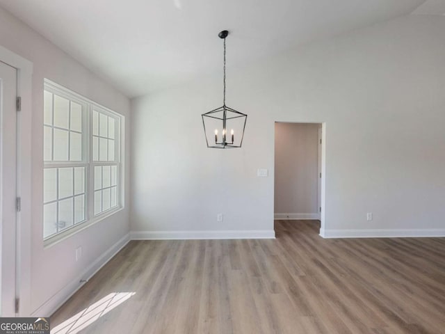 unfurnished dining area featuring baseboards, light wood-type flooring, a notable chandelier, and lofted ceiling