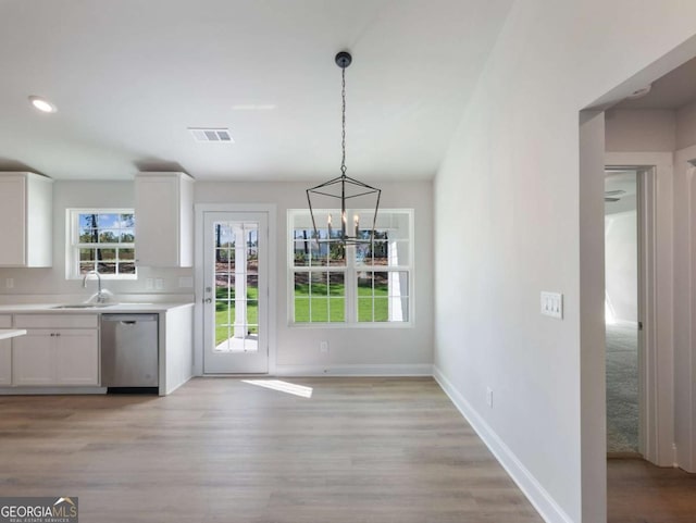 unfurnished dining area featuring light wood-style flooring, visible vents, a sink, baseboards, and a notable chandelier