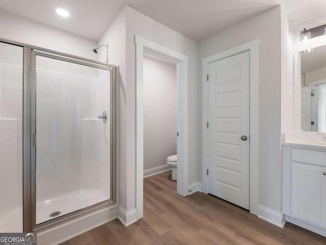 bathroom featuring vanity, toilet, wood finished floors, a stall shower, and baseboards