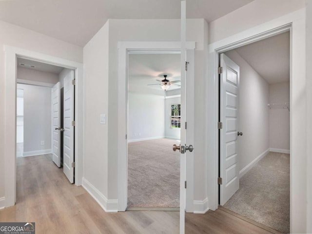 corridor featuring baseboards, light wood-type flooring, and light carpet