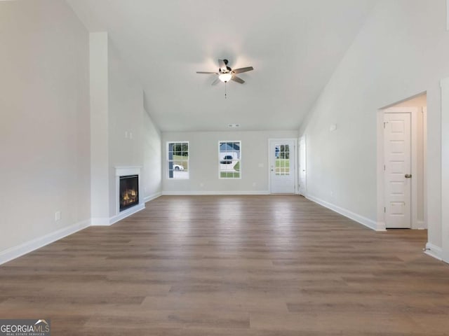 unfurnished living room with wood finished floors, a ceiling fan, a warm lit fireplace, and a wealth of natural light