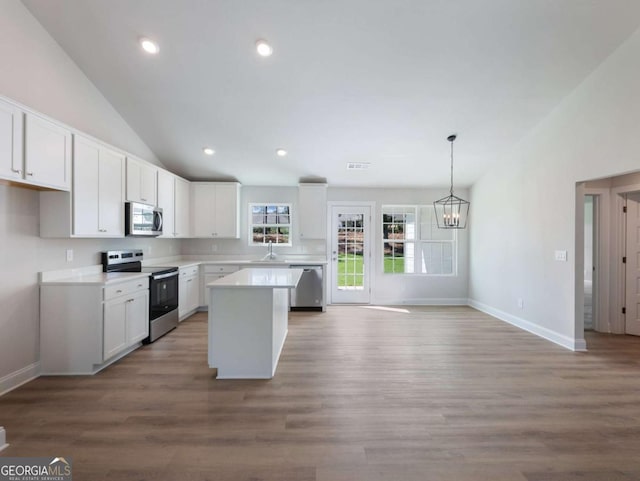 kitchen with an inviting chandelier, vaulted ceiling, a kitchen island, white cabinets, and appliances with stainless steel finishes