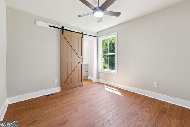 unfurnished bedroom with light wood-type flooring, a ceiling fan, visible vents, a barn door, and baseboards