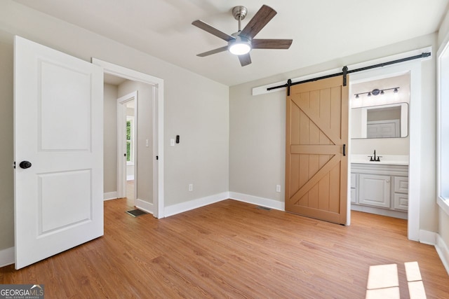 unfurnished bedroom with light wood-style floors, visible vents, a barn door, a sink, and baseboards