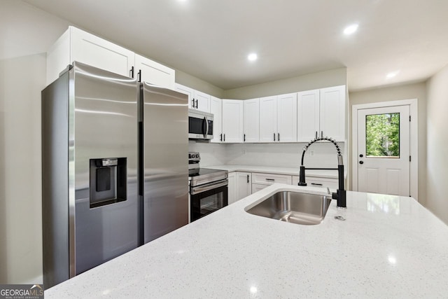 kitchen with recessed lighting, white cabinetry, light stone countertops, appliances with stainless steel finishes, and a sink
