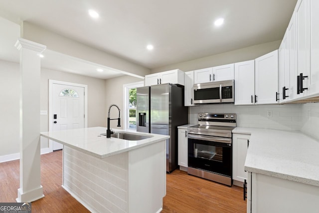 kitchen with tasteful backsplash, a sink, light wood-type flooring, appliances with stainless steel finishes, and a center island with sink