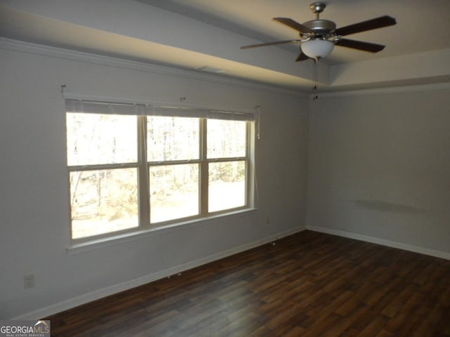 unfurnished room with crown molding, ceiling fan, dark wood finished floors, a tray ceiling, and baseboards