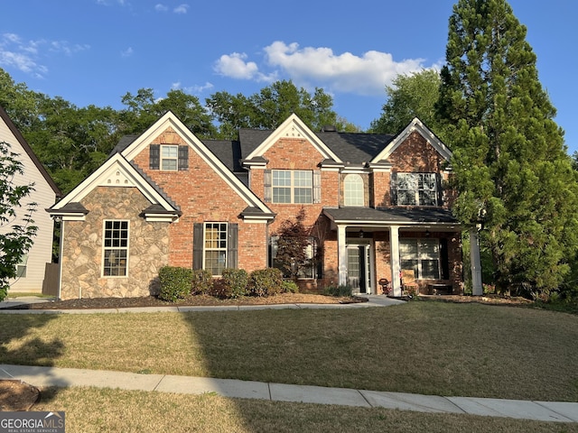 view of front of home featuring brick siding, stone siding, covered porch, and a front yard