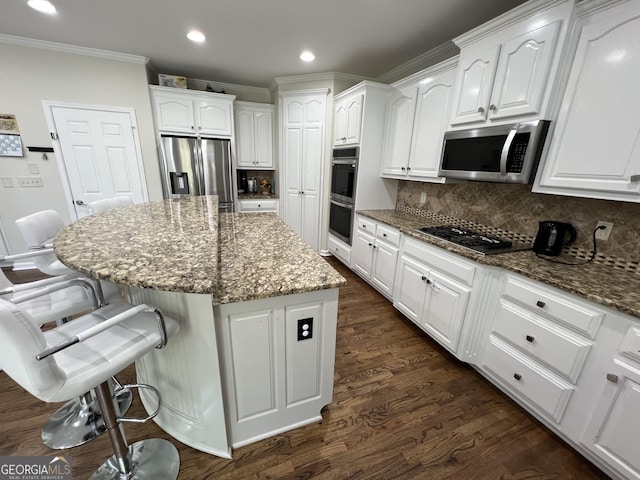 kitchen with stainless steel appliances, ornamental molding, stone counters, a kitchen island, and white cabinetry