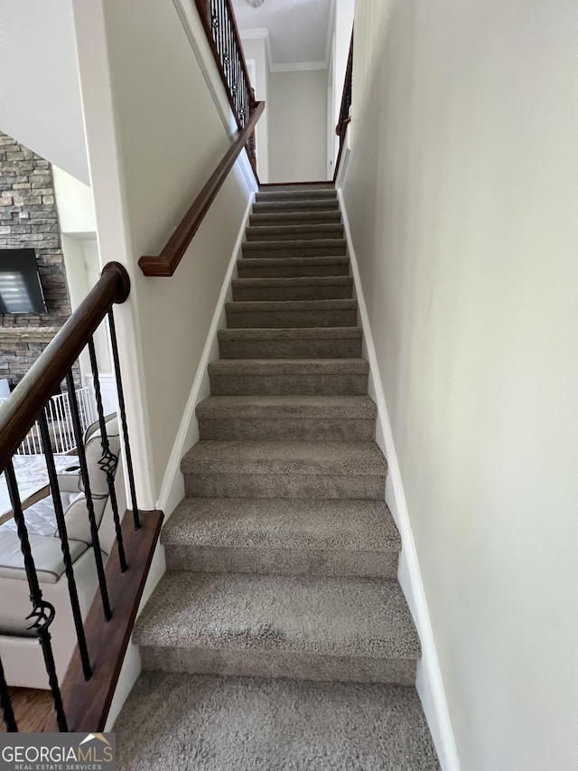 stairs featuring baseboards, a fireplace, carpet flooring, and crown molding