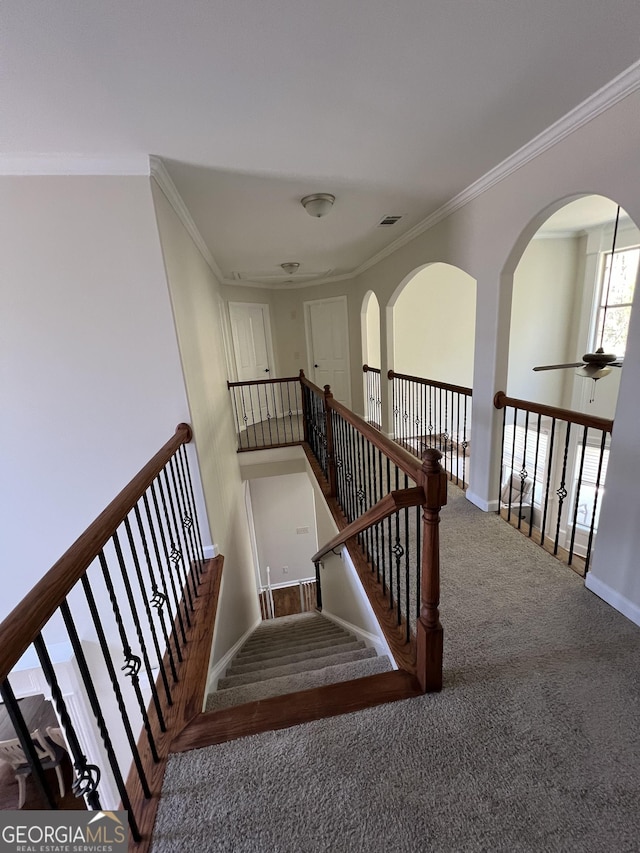 staircase featuring arched walkways, baseboards, ceiling fan, crown molding, and carpet floors