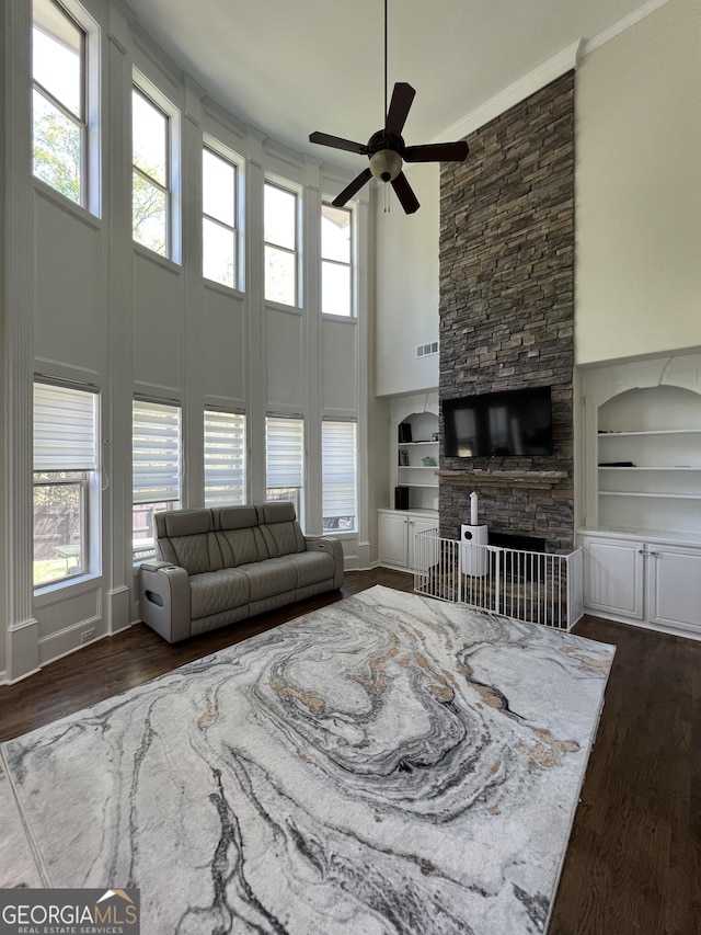 living room with built in shelves, dark wood-style flooring, a ceiling fan, and a high ceiling