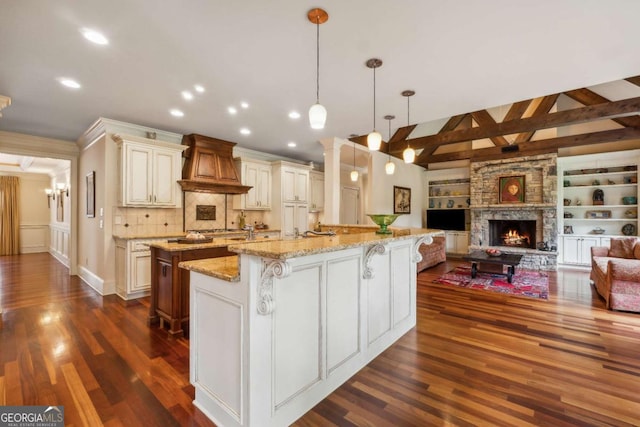6935 Wakehurst Pl, Cumming, GA 30040 - kitchen featuring premium range hood, a large island with sink, open floor plan, dark wood-style floors, and a stone fireplace