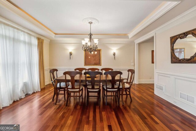 6935 Wakehurst Pl, Cumming, GA 30040 - dining area with dark wood-type flooring, a raised ceiling, ornamental molding, a chandelier, and wainscoting