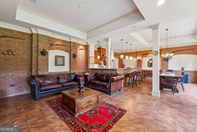 6935 Wakehurst Pl, Cumming, GA 30040 - living room featuring a tray ceiling, a chandelier, crown molding, brick wall, and tile patterned floors