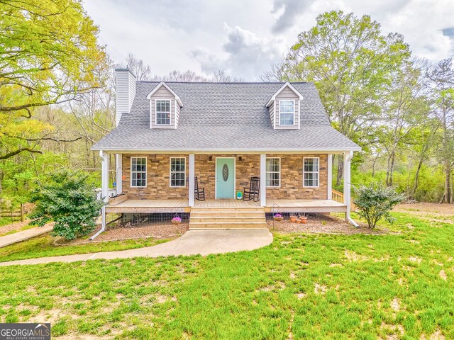new england style home featuring covered porch, stone siding, a front lawn, a chimney, and a shingled roof