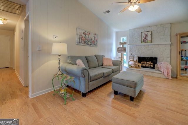 living room with visible vents, ceiling fan, a fireplace, vaulted ceiling, and wood finished floors