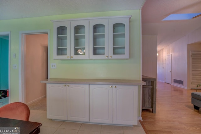 kitchen featuring visible vents, white cabinets, glass insert cabinets, baseboards, and a skylight