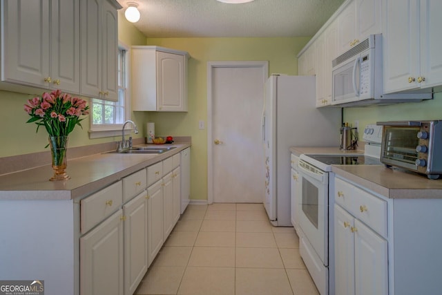 kitchen featuring light tile patterned floors, a sink, white appliances, and white cabinets