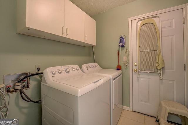clothes washing area with a textured ceiling, light tile patterned floors, washing machine and clothes dryer, and cabinet space