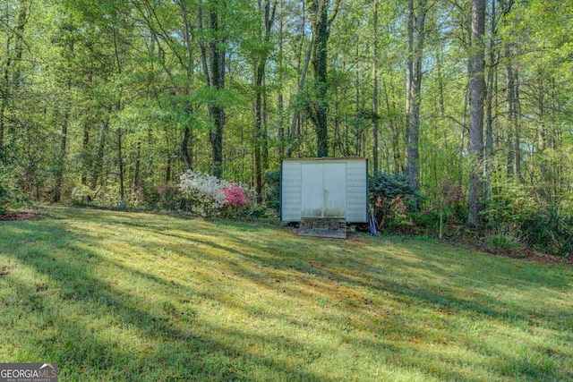 view of yard with a wooded view, an outbuilding, and a storage unit