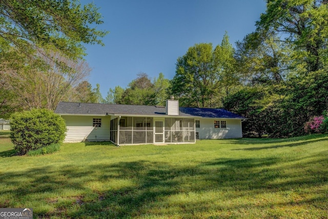 rear view of house with a sunroom, a lawn, and a chimney