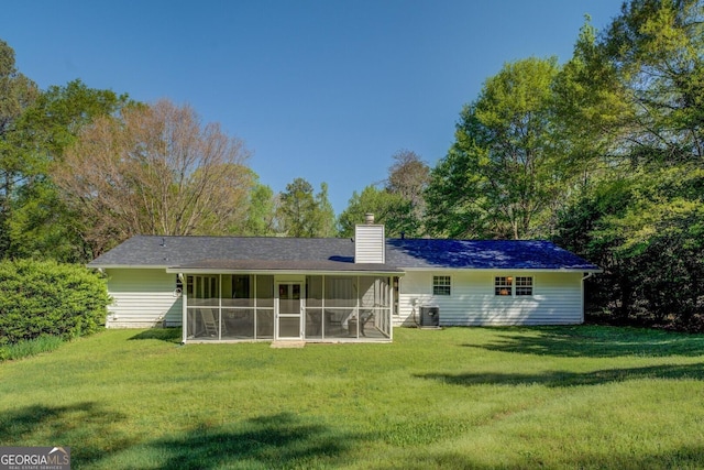 rear view of property featuring central air condition unit, a chimney, a sunroom, and a lawn