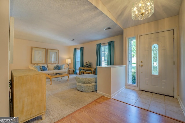foyer with visible vents, a notable chandelier, wood finished floors, and a textured ceiling