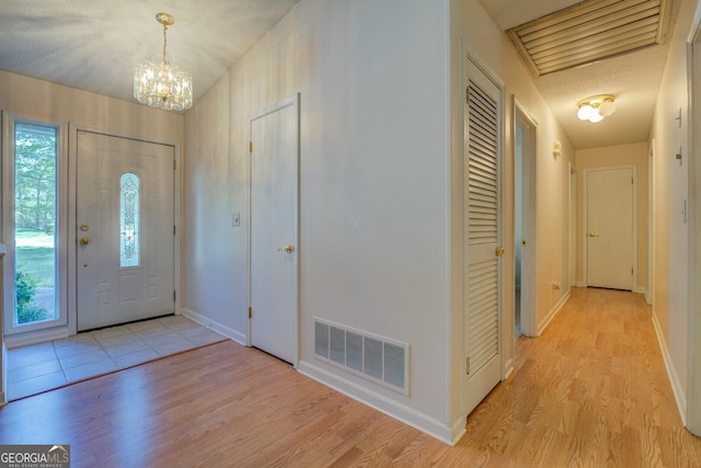 foyer with visible vents, an inviting chandelier, light wood-style floors, and a healthy amount of sunlight