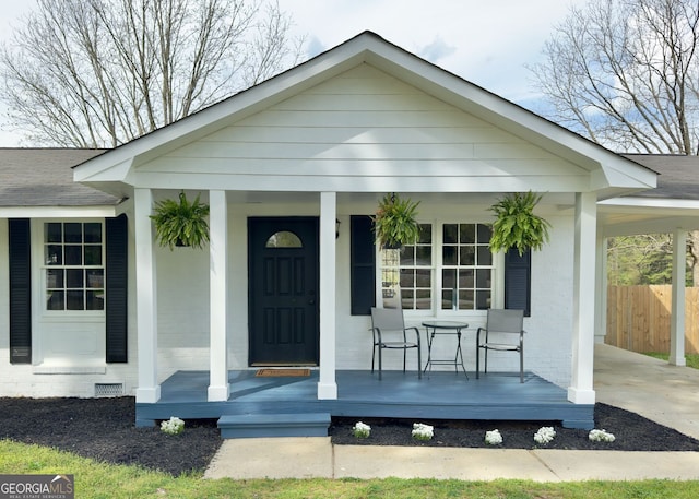 view of front of property featuring fence, roof with shingles, brick siding, an attached carport, and a porch