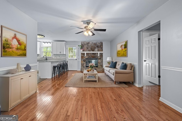 living area featuring light wood-style floors, baseboards, a fireplace, and a ceiling fan