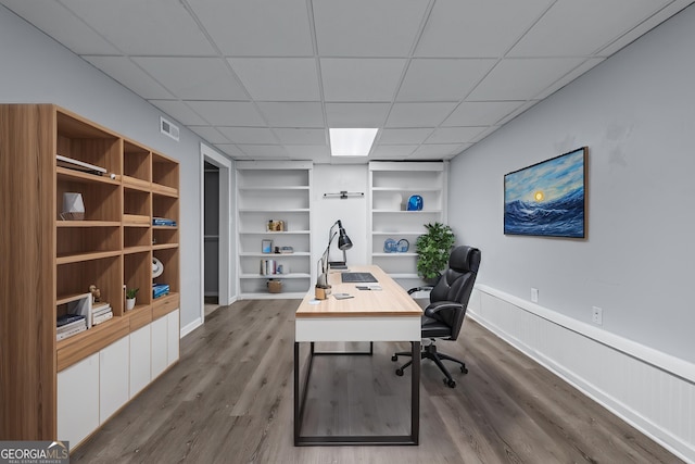 office space with a paneled ceiling, visible vents, built in features, a wainscoted wall, and dark wood-type flooring