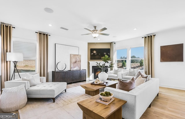 living room featuring a glass covered fireplace, baseboards, light wood-style flooring, visible vents, and ceiling fan