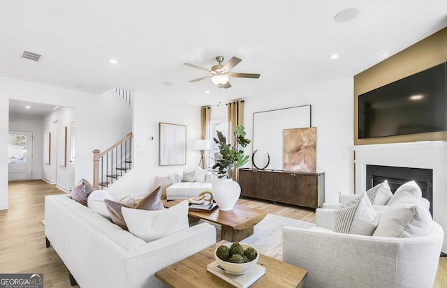 living room featuring light wood-type flooring, a ceiling fan, visible vents, recessed lighting, and stairs
