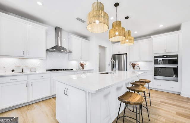 kitchen featuring light wood-style flooring, wall chimney range hood, stainless steel refrigerator with ice dispenser, a sink, and a breakfast bar area