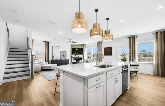 kitchen with white cabinets, a sink, open floor plan, light countertops, and light wood-style flooring