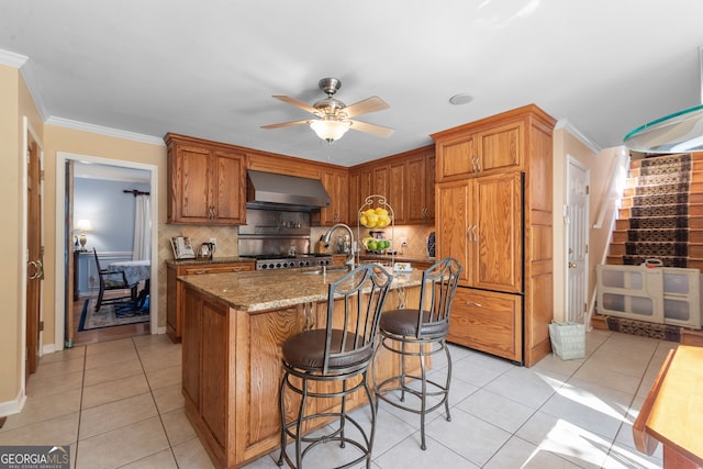 kitchen with wall chimney range hood, range, backsplash, light tile patterned floors, and crown molding