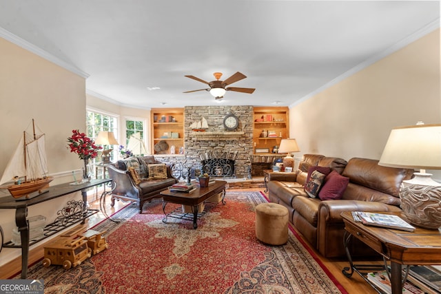 living room with wood finished floors, ceiling fan, built in shelves, crown molding, and a fireplace