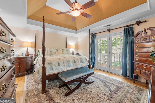 bedroom with a tray ceiling, access to outside, light wood-style flooring, ornamental molding, and a ceiling fan