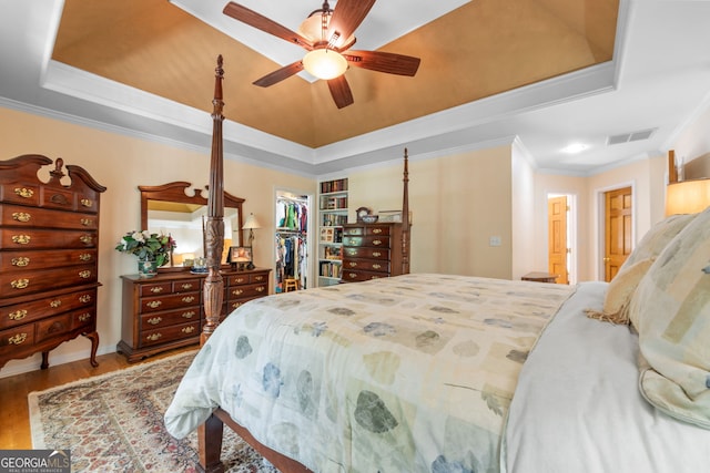 bedroom featuring a spacious closet, wood finished floors, a tray ceiling, crown molding, and a closet
