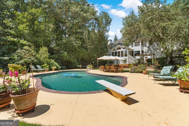 swimming pool with a patio, a diving board, and outdoor dining space