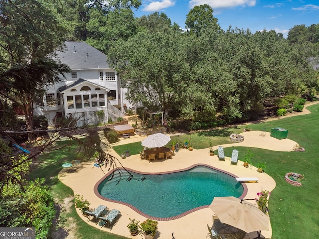 outdoor pool with a patio, a lawn, and a diving board