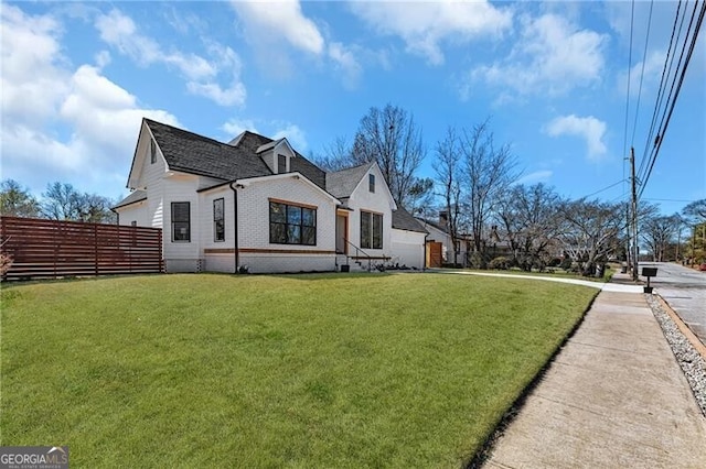 view of side of property with a yard, fence, and brick siding