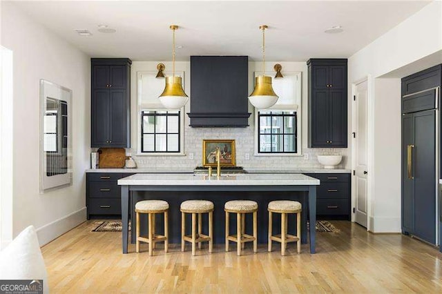 kitchen featuring custom range hood, light countertops, paneled refrigerator, and a breakfast bar area